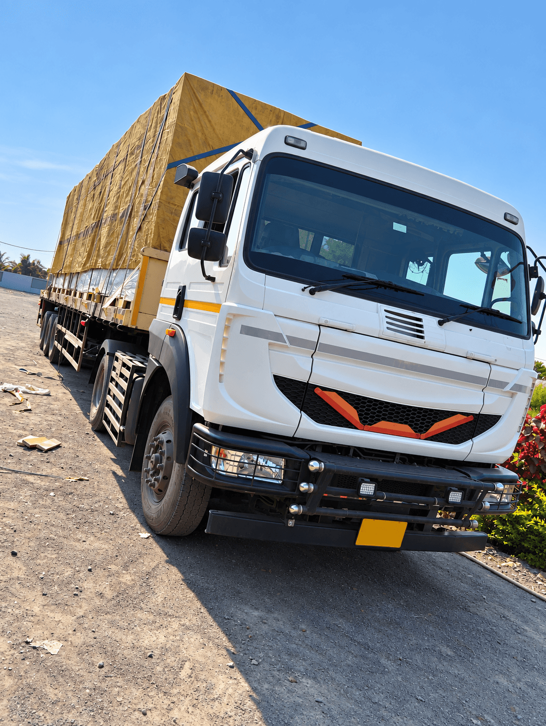 A white tractor unit coupled to a flatbed trailer carrying a tarpaulin-covered full load.